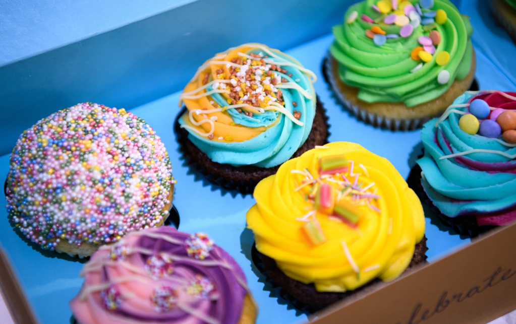 Very colourful photo of six fancy cupcakes; each one has a different colourful topping.