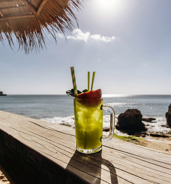 Photo of fancy cocktail on a wooden bench on a sunny beach